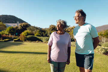 Multiracial senior friends looking away while standing on grassy land against clear sky in yard