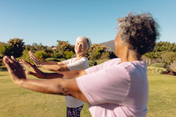 Smiling multiracial female seniors stretching hands against clear sky in yard at retirement home