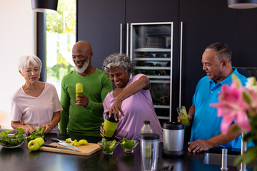 African american senior woman making smoothie for multiracial friends on kitchen counter - Powered by Adobe