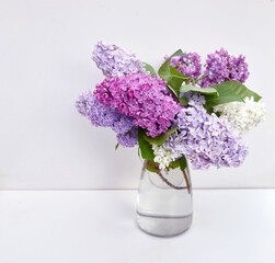 Lilac flowers bouquet in glass vase on white background.