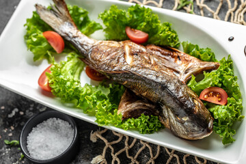 Dorado on grill and salad on a white plate on a dark background. top view. place for text