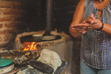 Mujer mexicana torteando maza de maíz en un metate y una estufa de leña para hacer tortillas...