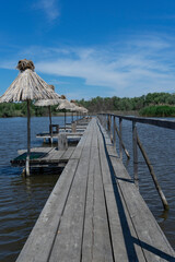 A wooden pier with small umbrellas on the lake against the backdrop of a forest and a blue sky with small clouds