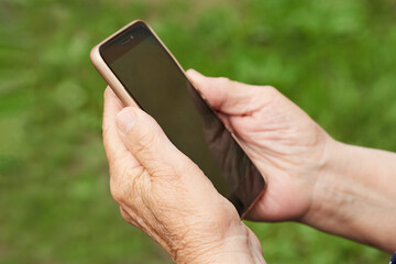 Hands of an elderly pensioner holding a smartphone outdoors