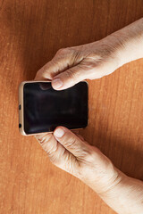Close up of senior woman's hands holding mobile phone on wooden table