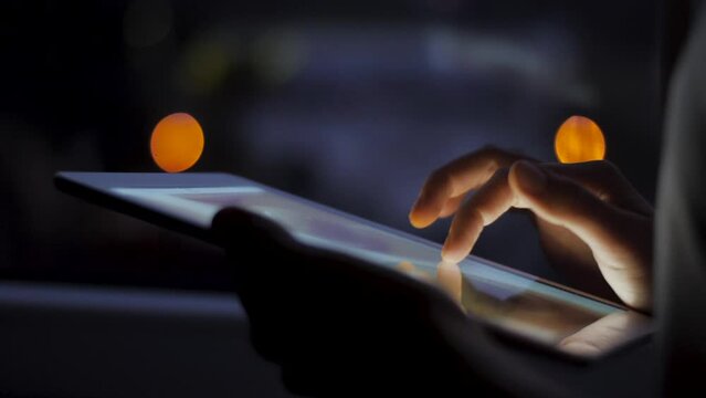 Girl swiping and scrolling ipad tablet screen late at night. Close up shot with beautiful bokeh lights in the background. Technology and communication related footage.