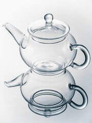 Empty transparent glass teapot on a mirror surface in cold tones. Studio shot. Close-up. Vertical.