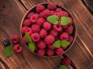 Fresh raspberries in a wooden bowl on a wooden table decorated with mint and lemon balm leaves Rustic. Flat lay. View from above. Flatly. 