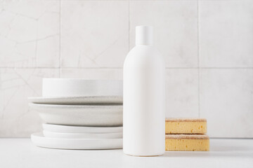 White bottle with dishwashing detergent and plates in the background. Washing dishes in the kitchen, cleaning concept