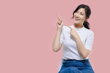 Happy young Asian woman feeling happiness and gesture pointing finger on isolated pink background...