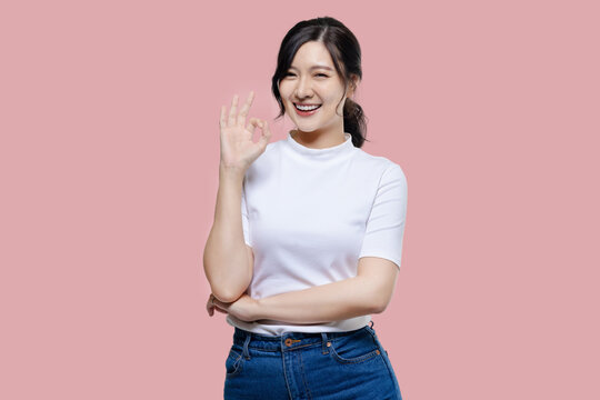 Happy young Asian woman feeling happiness and gesture showing OK hand sign on isolated pink background.