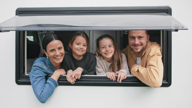 Happy young family with two children looking out of caravan window.