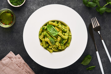 Italian Fusilli Pasta with Pesto. Fusilli pasta with basil pesto and herbs, parmesan cheese, basil and garlic on white plate on black stone countertop background. Top view. Copy space. Mock up.