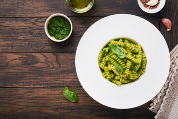 Italian Fusilli Pasta with Pesto. Fusilli pasta with basil pesto and herbs, parmesan cheese, basil and garlic on white plate on old wooden table background. Top view. Copy space. Mock up.