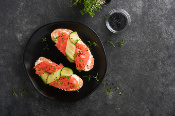 Sandwiches. Salmon toast with cream cheese, cucumber, black sesame and microgreens on black background. Seafood. Healthy food. Photography in low key. Top view.