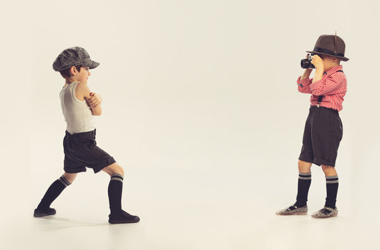 Portrait of two little boys, children palying together. Boy taking photo of his friend isolated over grey studio background