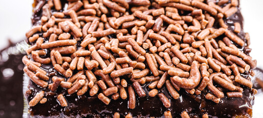 close up slice of carrot cake with creamy chocolate icing and sprinkles, typical of Brazilian June festivals