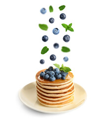 Fresh blueberries and mint leaves falling onto stacked pancakes against white background