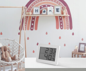 Digital hygrometer with thermometer on white table in children's room. Optimal humidity level for kids - obrazy, fototapety, plakaty