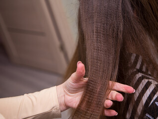 Close-up of a woman's hand holding a wavy strand of hair. The hairdresser makes a hairstyle for a young woman. Barber shop, business concept. Beauty salon, hair care.