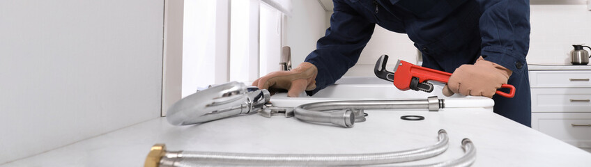 Professional plumber fixing water tap in kitchen, closeup. Banner design