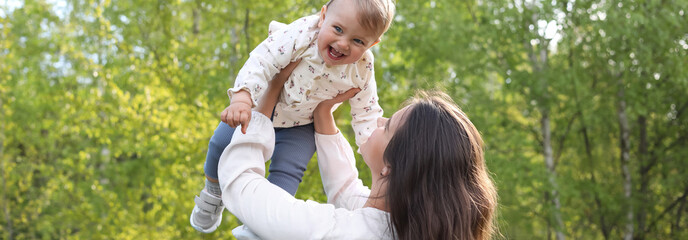 Happy mother playing with her cute baby in park on sunny day. Banner design