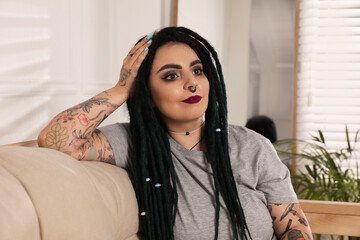 Beautiful young woman with tattoos on body, nose piercing and dreadlocks at home