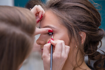 Close-up of the make-up artist's hands lead the eye arrows to the girl client. Female master makes makeup to a young woman. Business concept - beauty salon, facial skin care, cosmetology.