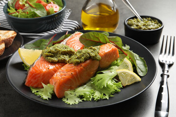 Tasty cooked salmon with pesto sauce served on dark grey table