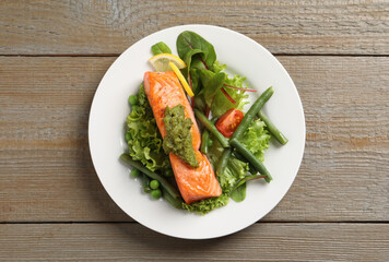 Tasty cooked salmon with pesto sauce and fresh salad on wooden table, top view