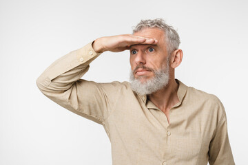 Pensive caucasian mature middle-aged man freelancer in casual clothes looking far away with his hand covering eyes, looking for new opportunities and plans for future isolated in white