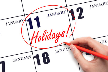 Hand drawing a red circle and writing the text Holidays on the calendar date 11 January. Important date.