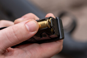 A male hunter loads cartridges for a rifle magazine on a blurry background, equips a combat weapon.