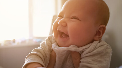 Cute newborn girl with plump cheeks smiles widely feeling happily at home. Mother holds baby with...