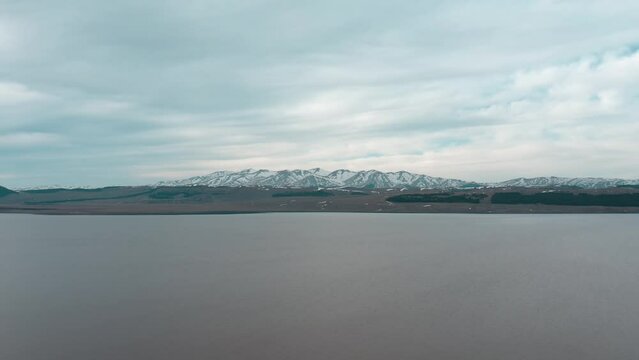 Calm Waters Of Paravani Lake In Javakheti Plateau, Georgia. Snowy Mountains In Background. wide ascending shot