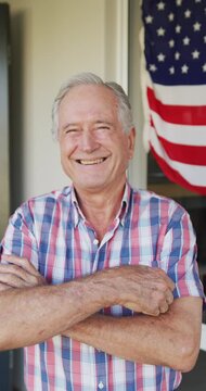 Vertical video portrait of happy caucasian senior man in front of house decorated with american flag