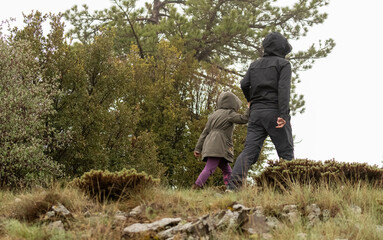 Selective focus shot of mother and daughter walking on dirt forest path in nature in foggy weather.