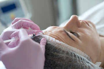 Close-up real process of the hands of an expert cosmetologist injecting botox into a woman's...