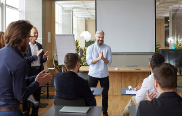 Proud male boss at team meeting in office applauds his subordinate congratulating him on job well...