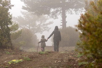 Mother daughter silhouette shot in foggy and hazy image on forest road in nature.