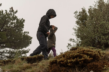 Selective focus shot of mother and daughter walking on dirt forest path in nature in foggy weather.
