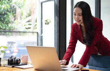 Fototapeta premium Portrait of Asian young female Businesswoman working on laptop computer doing finances,accounting analysis,report,data and pointing graph at the office.
