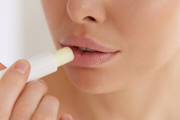 Lips care. Close up of young woman applying hygienic balm on her plump lips in studio. Charming lady using professional cosmetic for taking care of her soft skin. - obrazy, fototapety, plakaty