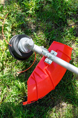 Reel of gas trimmer with fishing line, lawn mower on grass background. Trimmer head