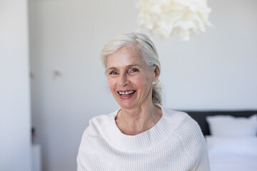 Portrait of caucasian senior woman smiling sitting on the bed at home