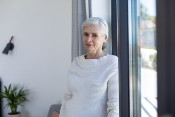 Portrait of caucasian senior woman smiling standing near the window at home