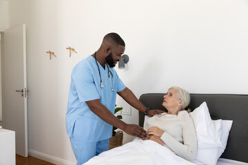 Obraz premium African american male health worker supporting caucasian senior woman lying on the bed at home
