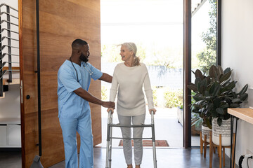 African american male health worker helping caucasian senior woman to walk with a walking frame