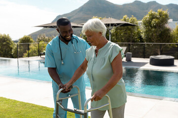 African american male health worker helping caucasian senior woman to walk with a walking frame