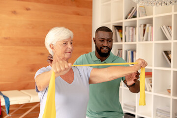African american male physiotherapist helping senior woman to exercise with resistance bands